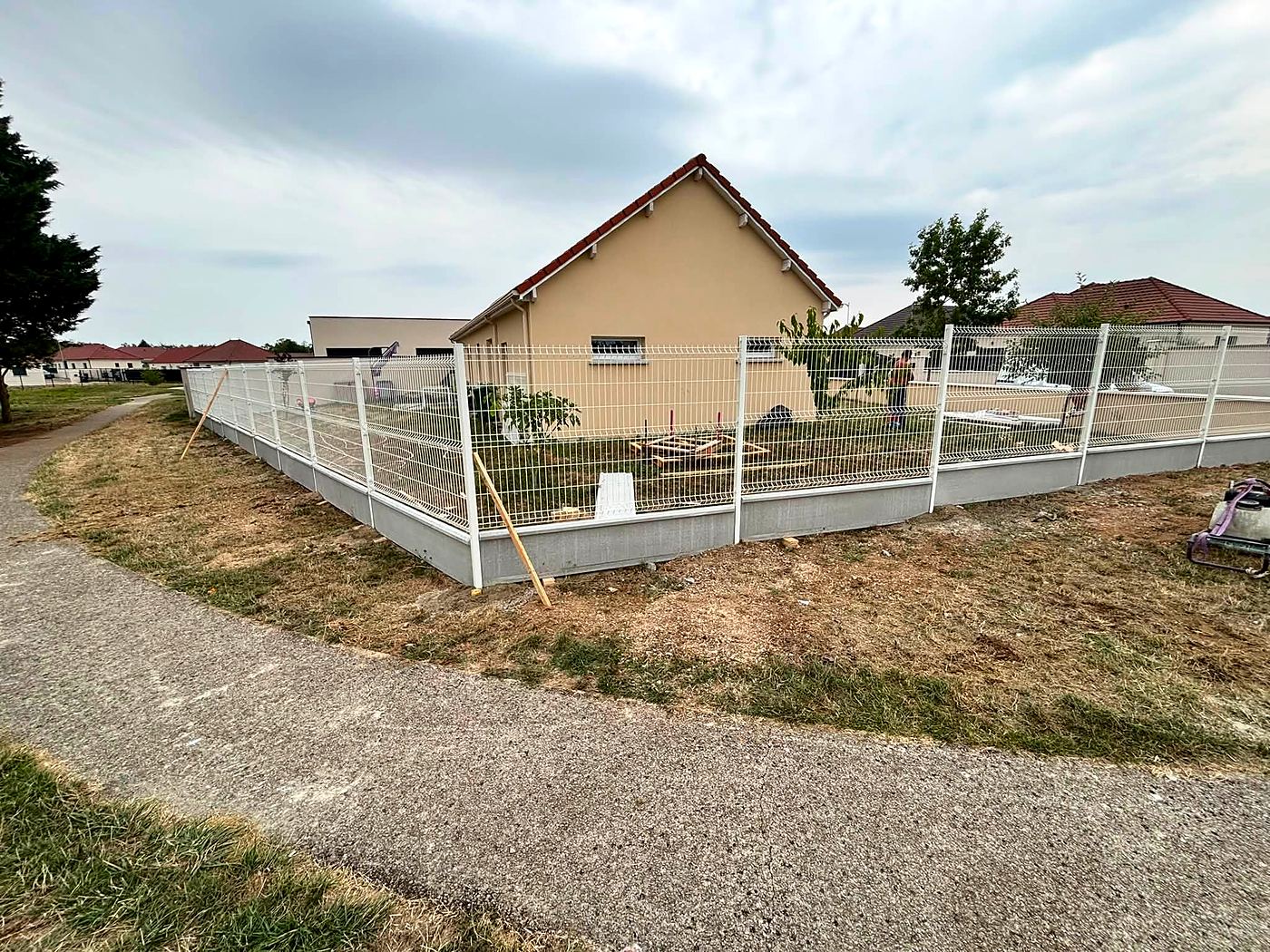 Clôture en panneaux rigides autour d'une maison, avec allée en gravier