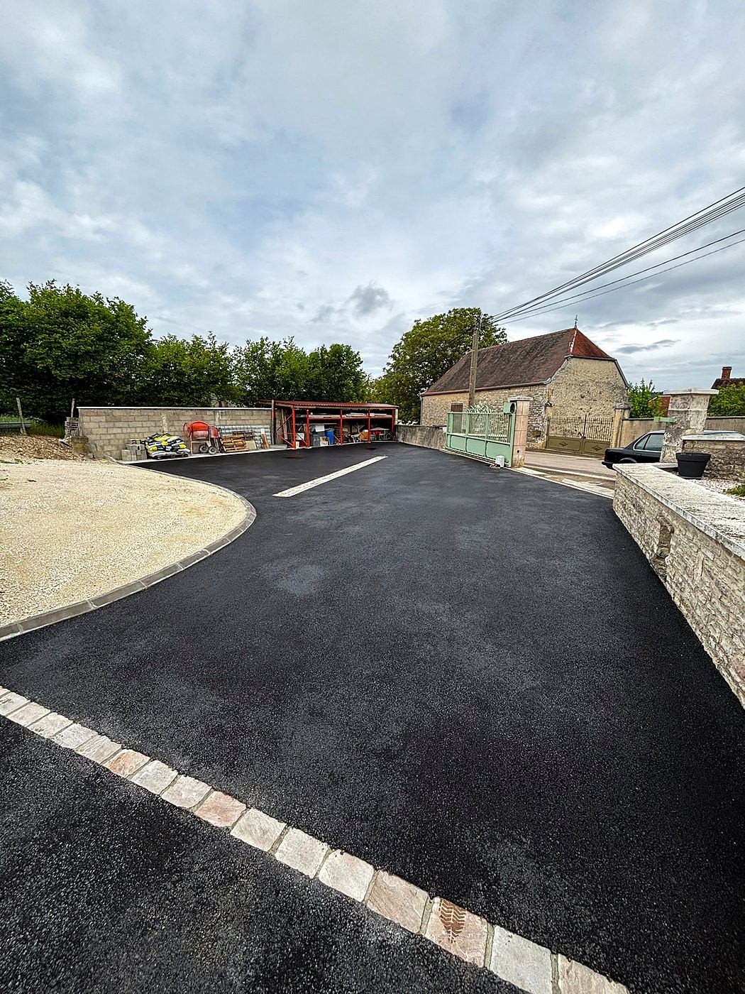 Cour en enrobé noir délimitée par une bordure en pavés